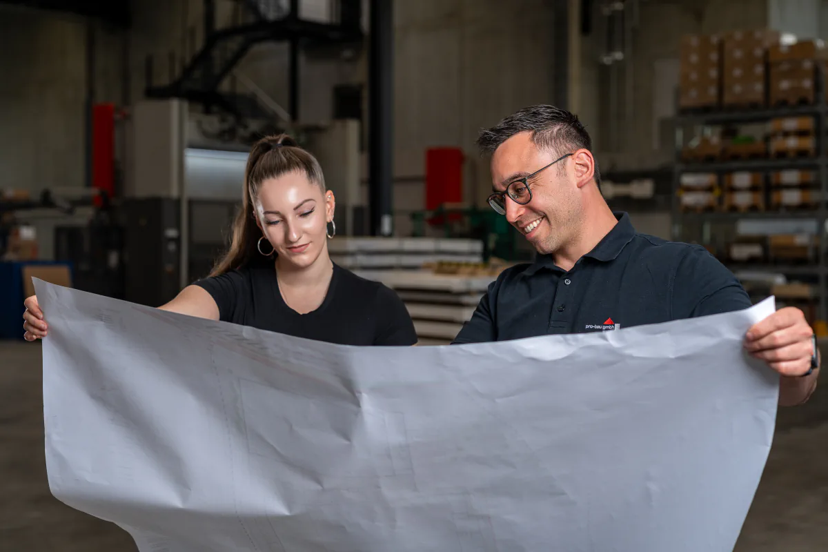 Zwei pro-bau Mitarbeitende prüfen gemeinsam einen Bauplan in der Halle